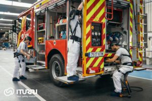 Des opérateurs portant des exosquelettes s'affairent autour d'un camion de pompiers.