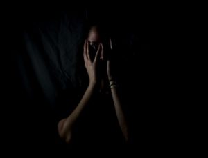 Une femme dans le noir cache son visage entre ses mains.