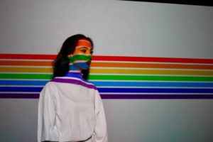 Une femme se tient devant un spectre aux couleurs LGBT.