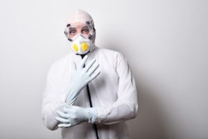 Un homme porte un masque respiratoire ainsi qu’une combinaison et des gants de protection.